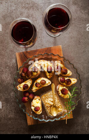 Rotwein und Vorspeise mit Häppchen mit Käse, Trauben, Wein, Honig und Brot auf einem Holztisch Stockfoto