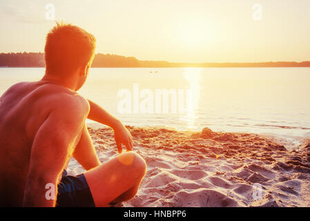 Mann sitzt am Strand bei Sonnenuntergang Stockfoto