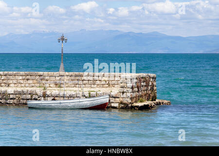 Kleine weiße Ruderboot festgemacht am steinernen Pier im Hafen von See Ohrid, Mazedonien Stockfoto