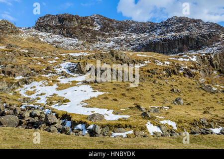 Felsige Berge mit Schneeflecken gesehen von der isolierten Straße zwischen Borrowdale und Watendlath im englischen Lake District auf Ende März Stockfoto