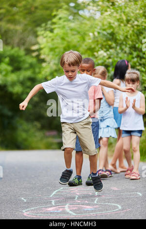 Junge, springen in Himmel und Hölle-Wettbewerb auf der Straße Stockfoto