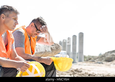 Müde Betreuer sitzen mit Kollegen auf Baustelle Stockfoto