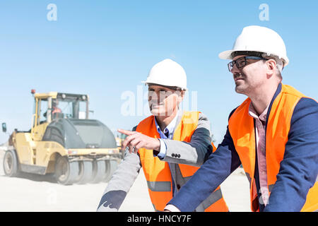 Vorgesetzten erklären Plan an Kollegen bei der Baustelle gegen klaren Himmel Stockfoto