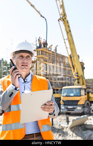 Männlichen Vorgesetzten mit Walkie-talkie gedrückter Zwischenablage auf Baustelle Stockfoto