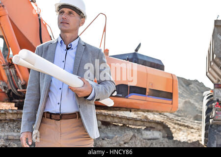 Zuversichtlich Architekt wegsehen gedrückter Blaupausen auf Baustelle Stockfoto