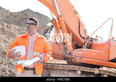 Zuversichtlich Architekten halten Bauarbeiterhelm und Baupläne auf Baustelle Stockfoto