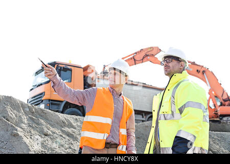 Ingenieur, zeigen etwas an Kollegen während der Diskussion auf Baustelle gegen klaren Himmel Stockfoto