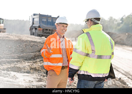 Glücklich Ingenieur im Gespräch mit Kollegen auf Baustelle am sonnigen Tag Stockfoto