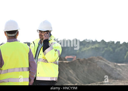 Vorgesetzten über Mobiltelefon stehend mit Kollegen bei der Baustelle gegen klaren Himmel Stockfoto