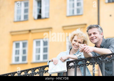 Glückliches Paar mittleren Alters mit Karte stützte sich auf Geländer gegen Gebäude Stockfoto