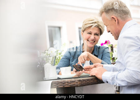 Glückliches Paar mittleren Alters mit Handy im Straßencafé Stockfoto