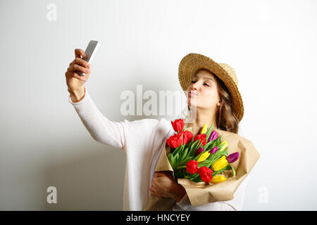 Junge Frau mit Küssen Lippen mit einem Blumenstrauß in der Hand und macht Selfie Foto Stockfoto