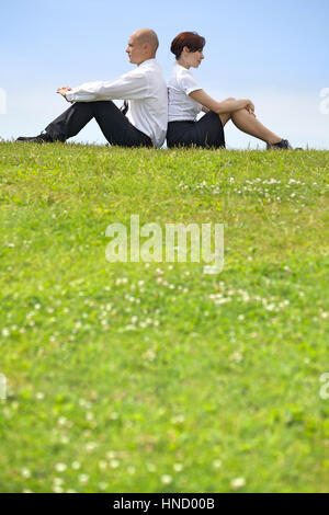 Geschäft paar sitzen Rücken an Rücken auf dem Rasen Stockfoto