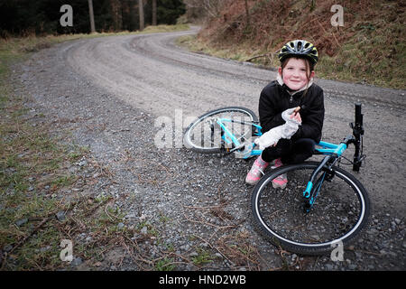 Ein junges Mädchen sitzt mit ihrem Fahrrad Essen einen Snack auf einen Waldweg Stockfoto