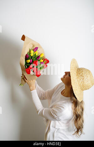 Frau mit einem Strauß Tulpen in Kraftpapier. Strohhut auf dem Kopf Stockfoto