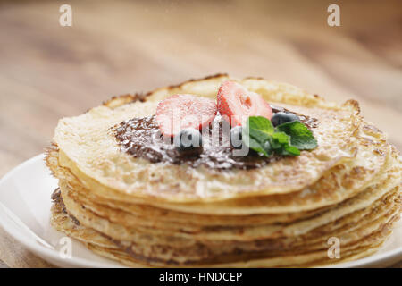 frische Blinis oder Plinsen geschmolzene dunkle Schokolade, Beeren und Zucker Pulver, flachen Fokus Stockfoto