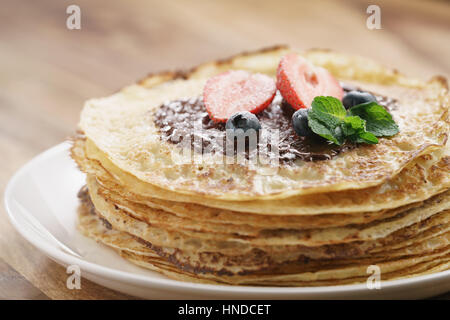 frische Blinis oder Plinsen geschmolzene dunkle Schokolade, Beeren und Zucker Pulver, flachen Fokus Stockfoto