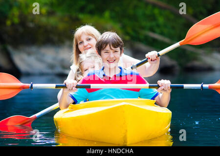 Glückliche Familie mit zwei Kindern Kajakfahrt auf schönen Fluss genießen. Mutter mit jungen Mädchen und Teenager Kajak an heißen Sommertag. Wasser-Sport-fu Stockfoto