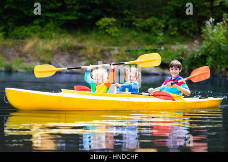 Glückliche Familie mit drei Kindern Kajakfahrt auf schönen Fluss genießen. Kleine Mädchen, Kleinkind Jungen und Teenager Kajak an heißen Sommertag. Wassersport und Stockfoto