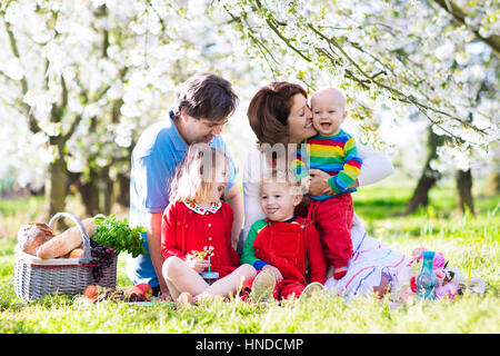 Große Familie mit drei kleinen Kindern beim Mittagessen im Freien. Eltern und Kinder mit Picknick-Korb im Frühlingsgarten. Mutter, Vater, Kind Mädchen, t Stockfoto