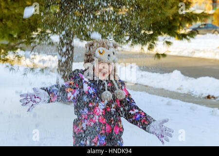 Reportageaufnahme ein kleines Mädchen bläst Schneeflocken aus ihren Händen im Freien an einem sonnigen Wintertag Stockfoto