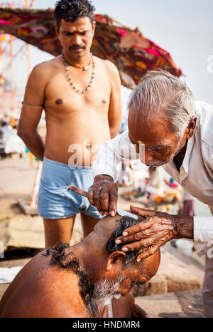 Baeber rasieren des Kopfes und Bart eines Pilgers, Dashashwamedh Ghat (Haupt-Ghat), im Fluss Ganges, Varanasi, Uttar Pradesh, Indien. Stockfoto