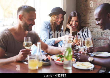 Gruppe von zwei Männchen und zwei Weibchen mit leckeren Abendessen während Mädchen teilen etwas am Telefon. Stockfoto