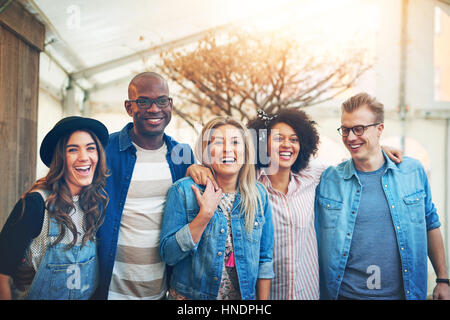 Gruppe von fünf schöne junge Menschen in Freizeitkleidung drinnen eng zusammenstehen, lachen und Lächeln zu Kamera posieren, Stockfoto