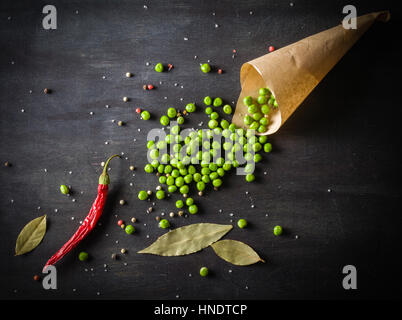 Grüne Erbsen in eine Papiertüte und Chilischoten auf einem dunklen Hintergrund aus Holz. Ansicht von oben Platz für text Stockfoto