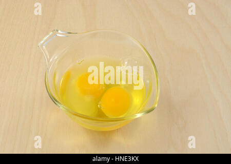 Zwei rohen Eiern in Glas Messbecher auf Holztisch Stockfoto