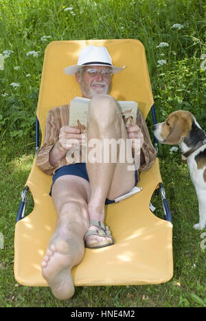 Model Release, Pensionist, 65 +, so Auf Liegestuhl Im Garten Und liest Ein Buch, Lebenswege Steht Sein Hund - Rentner auf einem Liegestuhl liegen und readin Stockfoto