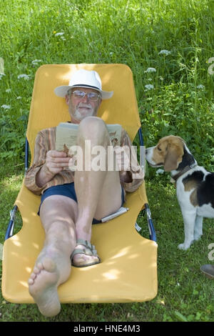 Model Release, Pensionist, 65 +, so Auf Liegestuhl Im Garten Und liest Ein Buch, Lebenswege Steht Sein Hund - Rentner auf einem Liegestuhl liegen und readin Stockfoto