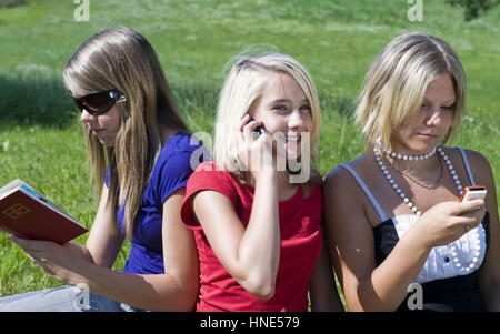 Model Release, Drei Jugendliche näher einer Mit Buch Und dann in der Wiese - drei Mädchen im Teenageralter sitzen mit Mobiltelefonen und buchen auf Wiese Stockfoto