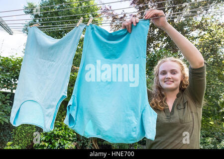 Kaukasischer Teenager-Mädchen hängt Kleidung auf der Wäscheleine draußen Stockfoto