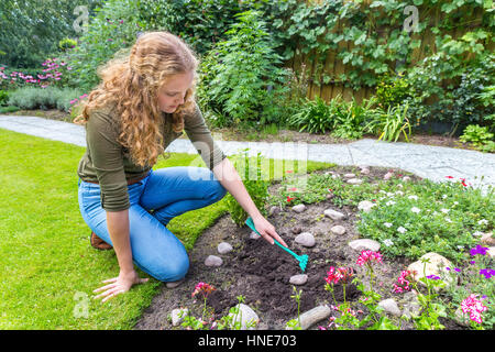 Niederländische Teenager-Mädchen mit Rechen draußen im Garten arbeiten Stockfoto