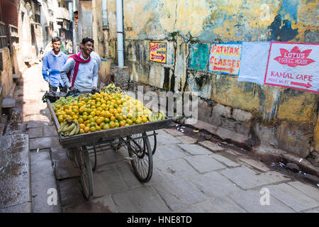 Ein Mann verkauft Bananen und Orangen aus einem Warenkorb in einer Gasse in Varanasi, eine der heiligsten Städte Indiens. Stockfoto