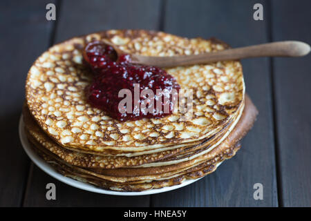 Hausgemachte Pfannkuchen mit Himbeeren Marmelade auf einem dunklen Holztisch. Ansicht von oben mit Händen. Faschingsdienstag. Stockfoto