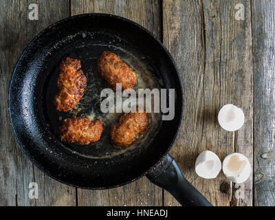 Zubereitung von Schnitzel. Pfanne mit gebratenen Koteletts auf einem alten verwitterten Holztisch Stockfoto