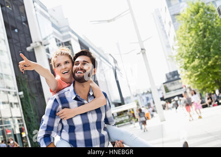 Glückliche Frau zeigen etwas zu Mann und genießen Huckepack Fahrt in die Stadt Stockfoto
