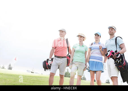 Männliche und weibliche Freunde am Golfplatz gegen klaren Himmel stehen