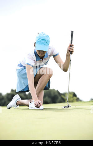 Junge Frau platzieren Ball kniend am Golfplatz Stockfoto