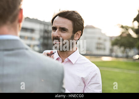 Unternehmer im Gespräch mit Kollegen im Park am sonnigen Tag Stockfoto