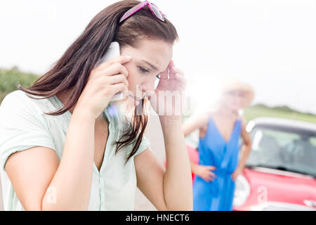 Besorgt Frau mit Handy während der Freund steht mit dem aufgeschlüsselt Auto an sonnigen Tag Stockfoto