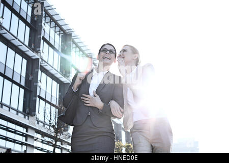 Glücklich Geschäftsfrau Kollegen Ohr außerhalb Bürogebäude am sonnigen Tag zu flüstern Stockfoto