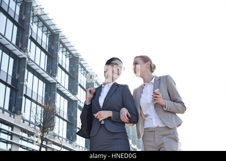 Niedrigen Winkel Ansicht glücklich Geschäftsfrauen zu Fuß außerhalb Bürogebäude gegen klaren Himmel Stockfoto