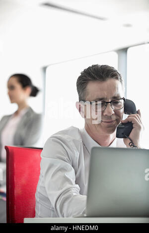 Geschäftsmann mit Kollegen im Hintergrund im Büro am Telefon sprechen Stockfoto