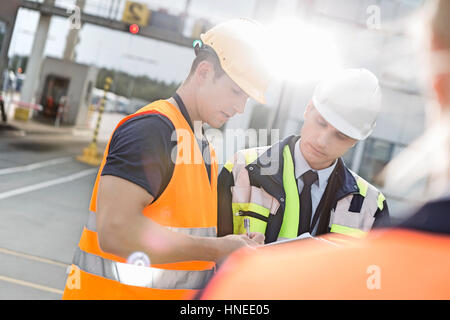 Männliche Arbeiter über Zwischenablage im Frachthafen diskutieren Stockfoto