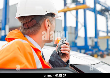 Mann mittleren Alters mit Walkie-talkie stehend neben Auto im Frachthafen Stockfoto