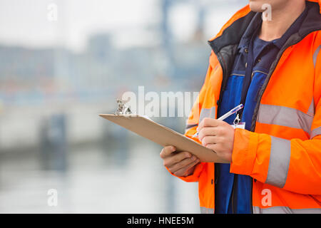 Mittelteil der Mitte erwachsenen Mannes in Zwischenablage im Frachthafen schreiben Stockfoto