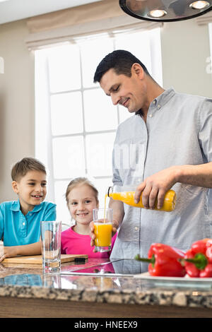 Vater mit Orangensaft für Kinder in Küche Stockfoto